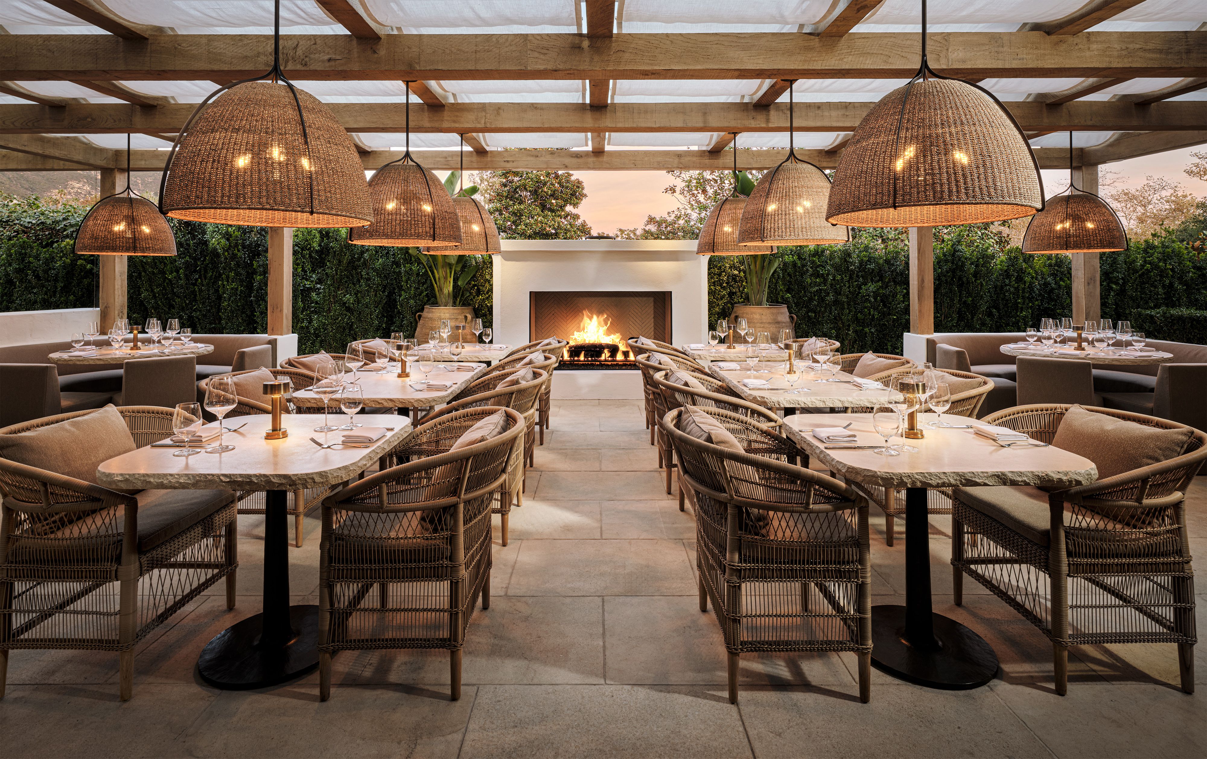Large tables are set in front of a glowing fireplace with luxury lighting and flooring at the new RH Firehouse Grill.
